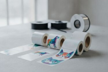 Rótulos adesivos para pet food em BOPP dispostos sobre mesa industrial com bobinas de ribbon de transferência térmica ao fund